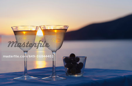 Two wine glasses and olives with sea in background