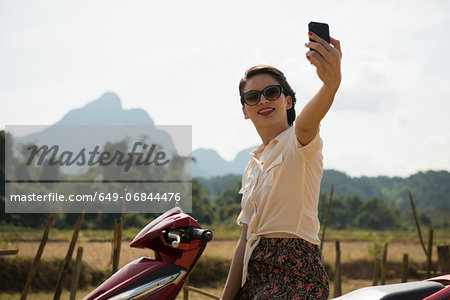 Woman photographing self on moped, Vang Vieng, Laos