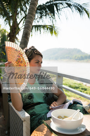 Woman sitting in cafe holding fan