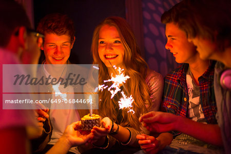 Group of teenagers sitting around birthday cake with sparklers