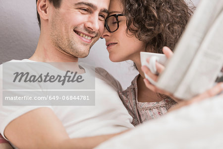 Mid adult couple reading newspaper in bed, face to face