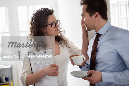Woman holding clipboard and touching face of mature man wearing shirt and tie holding cup of coffee