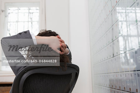 Woman sitting in office chair in front of large wall calendar