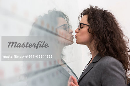 Businesswoman kissing her reflection on wall