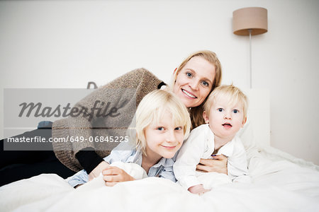 Portrait of mother and two young sons lying on bed