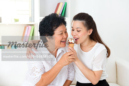 Sharing food. Happy Asian family sharing an ice cream at home. Beautiful senior mother and adult daughter eating dessert together.