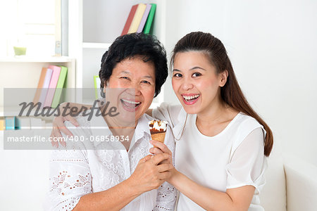 Sharing an ice cream. Happy Asian family sharing food at home. Beautiful senior mother and adult daughter eating dessert together.