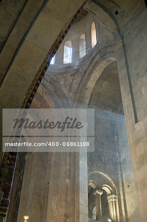 This is indoor scene of ancient Svetitskhoveli Cathedral in Mtskheta. Shoots of sunlight penetrate interior space of church.