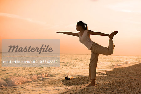 girl silhouette performing yoga on beach during a beautiful sunset