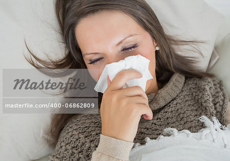 Sick woman lying on sofa and blowing nose in the living room