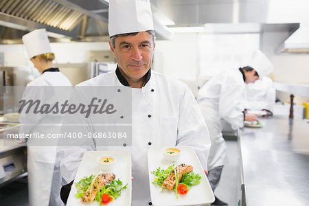 Chef holding out two salmon dishes in the kitchen