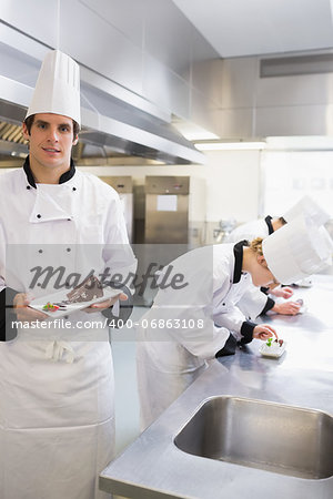 Chef presenting desert with others working on deserts in the kitchen