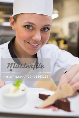 Smiling chef garnishing a slice of cake with wafers in the kitchen