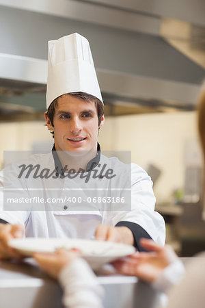 Chef passing plate to waitress at order station in kitchen