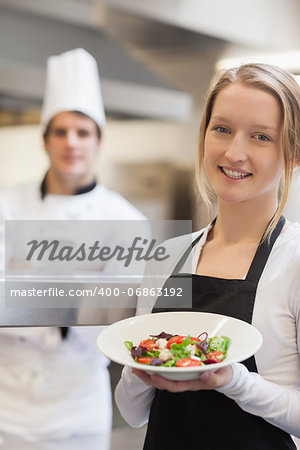 Waitress presenting a salad with chef behind her in kitchen