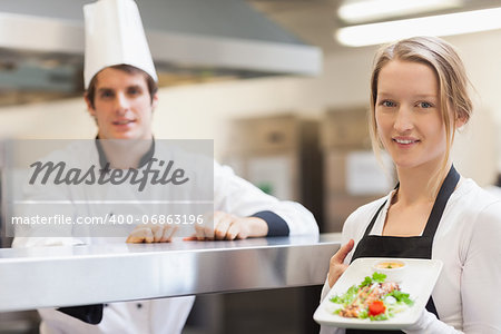Waitress holding salmon dish smiling with chef in the kitchen