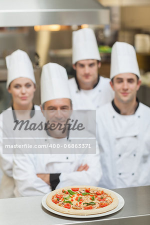 Pizza on the counter with team of Chef's behind in kitchen