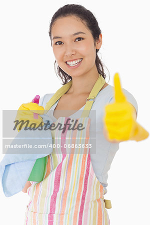 Smiling woman in apron holding cleaning products giving thumbs up