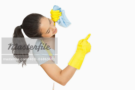 Happy woman pointing to white surface she is cleaning wearing rubber gloves and apron