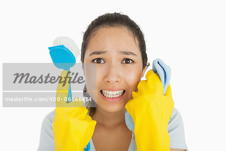 Distressed woman holding cloth and scrubbing brush in apron and rubber gloves