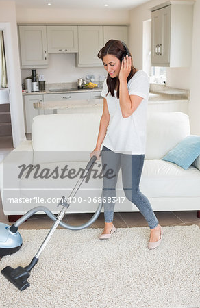 Woman standing holding a vacuum cleaner while wearing headphones  in the living room at home