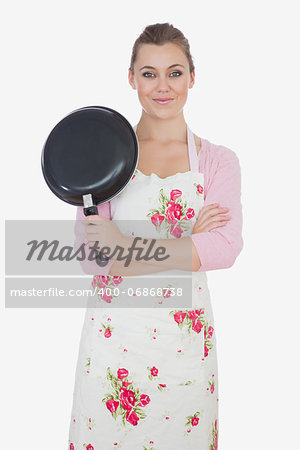 Portrait of beautiful young woman with arms crossed holding frying pan over white background