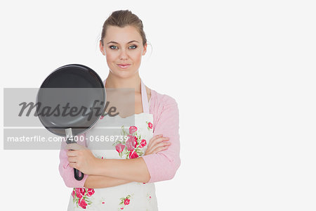 Portrait of young woman in apron holding frying pan over white background