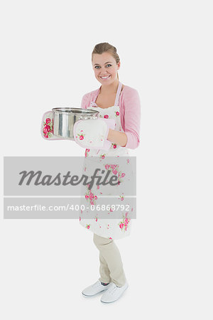 Full length portrait of young maid in apron holding utensil against white background