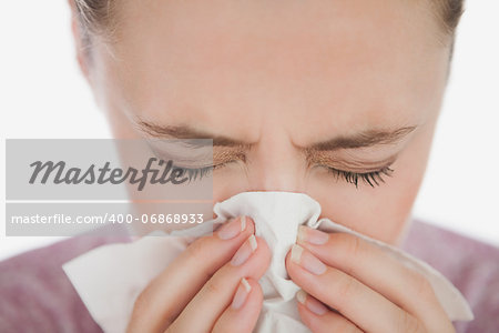Woman with eyes closed blowing her nose against white background