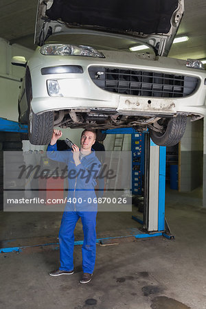 Full length portrait of male mechanic working under raised car in workshop
