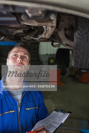 Young male mechanic with clipboard examining car in garage