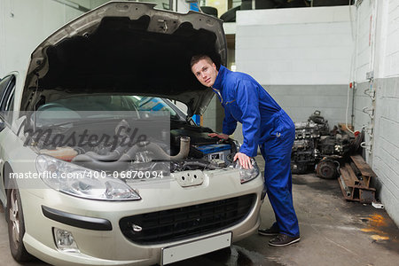 Portrait of young male mechanic examining car engine in workshop