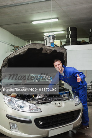 portrait of male mechanic by car giving thumbs up gesture