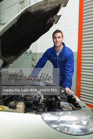 Portrait of male mechanic standing by car in workshop