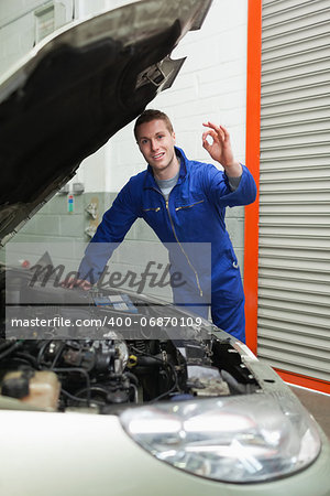 Portrait of young male mechanic by car making ok sign