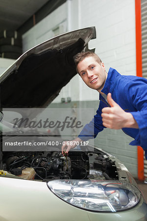 Portrait of auto mechanic gesturing thumbs up as he checks oil level of car