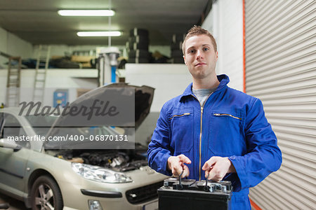Portrait of male mechanic carrying car battery in workshop
