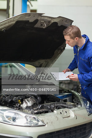 Male mechanic with clipboard checking car engine