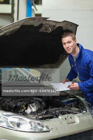 Portrait of auto mechanic with clipboard inspecting car engine