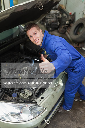 Portrait of auto mechanic by car showing thumbs up sign