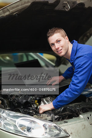Portrait of happy car mechanic with laptop checking engine