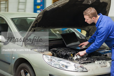 Male mechanic with laptop checking car engine