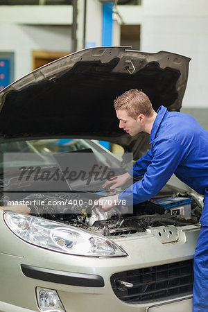 Auto mechanic with laptop repairing car engine in workshop