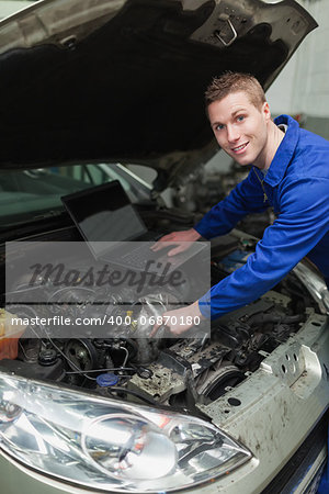 Portrait of happy mechanic with laptop repairing car engine