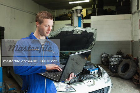 Male mechanic using laptop in garage with car in background