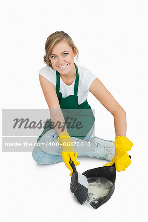 Portrait of smiling young maid using brush and dust pan over white background