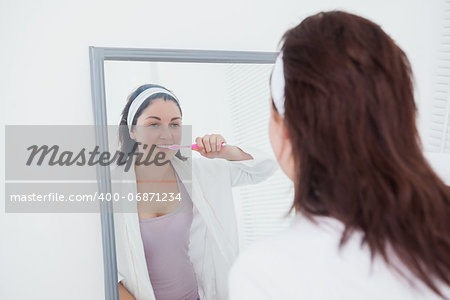 Young woman brushing teeth in bathroom mirror