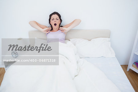 Sleepy young woman sitting and yawning in bed