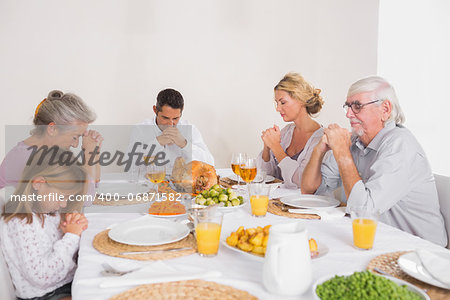 Family saying grace before eating a turkey for dinner