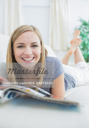 Portrait of casual young woman with magazine lying on couch at home